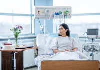 Young female patient recovering in hospital bed with monitoring equipment and meal tray.&nbsp;