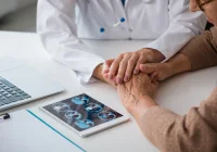 Doctor holding patient&#039;s hand during consultation with brain MRI scans displayed on tablet.&nbsp;