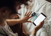 Woman uses pulse oximeter and smartphone for remote health monitoring at home.&nbsp;