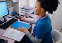 Female healthcare professional updating electronic medical records at a clinic workstation.