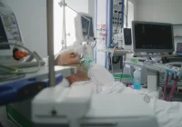 Critically ill patient on ventilator in intensive care unit surrounded by vital signs monitoring equipment.&nbsp;