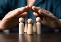 Hands shielding wooden figures symbolising protection, safety, and social care support&nbsp;