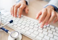 Doctor typing on keyboard with stethoscope nearby, managing electronic health records (EHR)&nbsp;
