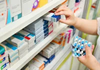 Pharmacist selecting medicine from pharmacy shelves while holding blister pack of pills&nbsp;