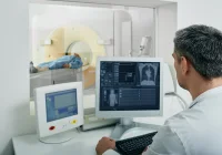 Radiologist monitoring CT scan procedure with patient inside scanner and chest images on screen