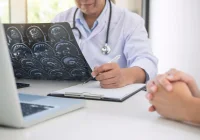 Doctor reviewing brain MRI scans and taking notes during patient consultation.&nbsp;