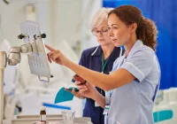 Senior nurse mentoring colleague while reviewing patient data on hospital monitor.&nbsp;