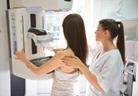 Radiographer positions patient at a digital mammography machine for breast cancer screening in a hospital imaging suite. 