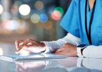 Healthcare professional in scrubs using a digital tablet, representing electronic health records and digital workflow in clinical care.&nbsp;