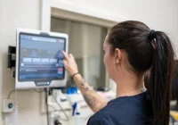 Healthcare professional accessing or updating patient data on a digital touchscreen system in a clinical environment.&nbsp;
