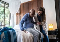 Caregiver&nbsp;assisting&nbsp;an older man to stand up from a bed at home.&nbsp;
