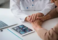 Doctor holding patient&#039;s hand during consultation with brain MRI scans displayed on tablet.&nbsp;
