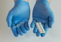 Gloved hands holding injection ampoule and blister pack of tablets, symbolising choice between oral and injectable medication.&nbsp;
