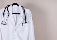 White doctor&rsquo;s coat with stethoscope hanging on hanger symbolising healthcare profession.&nbsp;
