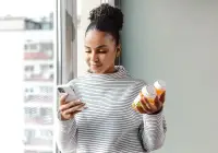 Young woman holding prescription pill bottles while using smartphone for digital health or pharmacy app&nbsp;