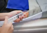 Healthcare worker holding a large syringe connected to a feeding or suction tube.&nbsp;