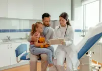 Paediatric&nbsp;consult: doctor reviews information on a tablet with a father and&nbsp;child&nbsp;holding a toy in a clinic.&nbsp;