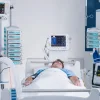 Patient in an intensive care setting surrounded by monitoring systems and infusion equipment, illustrating critical care management, continuous vital sign monitoring and technology-supported clinical intervention.