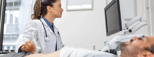 A female doctor performs an abdominal ultrasound on a male patient while checking the results on the screen.
