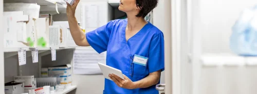 Nurse managing medical supplies and inventory using a digital tablet in a hospital storage room.