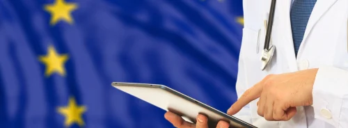 Doctor using a tablet in front of the EU flag, representing European healthcare policy and health regulation.
