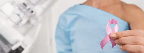 Patient holding a pink ribbon in a mammography clinic, symbolising breast cancer awareness, screening and early detection.