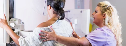 Technologist assisting patient during mammogram exam in a breast imaging clinic.