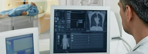 Radiology technician monitoring a patient undergoing a CT scan from a control room.