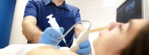 Clinician performing an ultrasound-guided procedure while monitoring imaging on a screen.