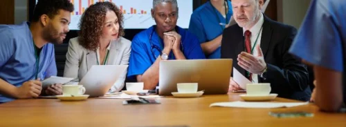 Multidisciplinary healthcare leadership team reviewing performance data and hospital strategy in executive meeting.