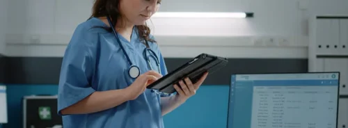 Nurse using a tablet in a hospital ward, illustrating digital healthcare workflows and clinical data access at the point of care.