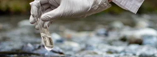 Scientist collecting a water sample in a test tube, illustrating environmental monitoring and public health risk assessment.