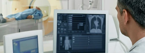 Radiologist monitoring imaging acquisition during a CT examination, illustrating real-time image review, workflow coordination and integration of diagnostic imaging systems in clinical practice.