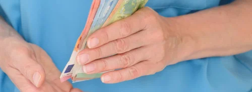 Healthcare worker handling euro banknotes, illustrating hospital finance, staff payments, healthcare costs and workforce funding.