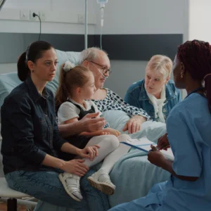 Family speaking with a nurse at a hospital bedside, representing patient-centred care and clinical communication.