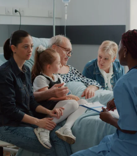 Family speaking with a nurse at a hospital bedside, representing patient-centred care and clinical communication.
