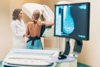 Female patient undergoing mammogram screening with breast scan image on monitor 