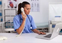 Smiling medical receptionist talking on the phone at a hospital front desk, highlighting healthcare communication, administrative efficiency and patient coordination. 