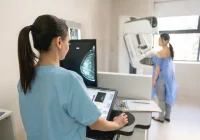 Female patient undergoing mammogram for breast cancer screening with technician reviewing imaging results 