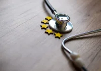 Healthcare quality concept with stethoscope and five-star rating symbol on wooden background. 