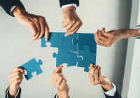 Business team collaborating to assemble puzzle pieces, symbolising teamwork and strategic collaboration. 