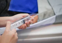 Close-up of hands holding a 60 mL syringe in a clinical setting.