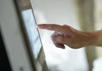 Close-up hand tapping a touchscreen kiosk, finger pressing digital interface. 