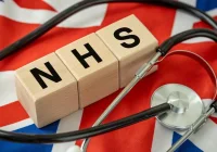 NHS wooden blocks with a stethoscope on a UK flag background.