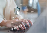 Hands typing on a laptop with a digital security overlay, representing healthcare cybersecurity and data privacy protection.