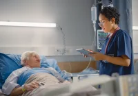 Nurse reviewing patient data at bedside, illustrating clinical monitoring and personalised inpatient care management.