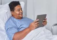 Hospital patient using a tablet, supporting digital patient engagement, remote monitoring and connected care.