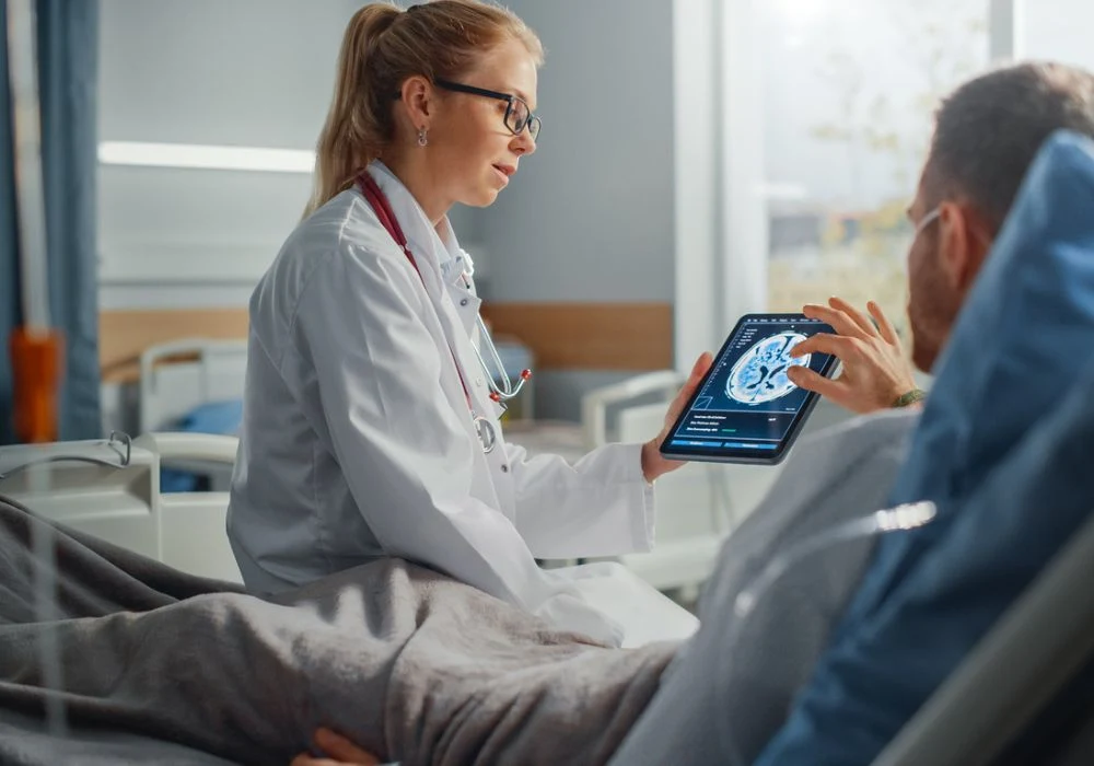 Doctor discussing brain scan results with male patient using digital tablet in hospital room