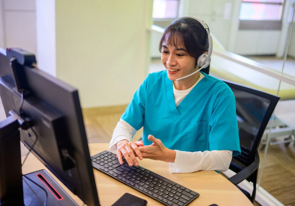 Smiling nurse providing telehealth support through computer and headset 