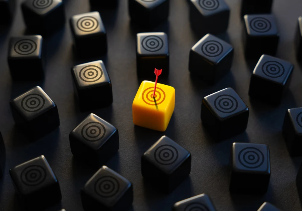 Yellow target cube with bullseye hit by dart among black cubes symbolising precision, accuracy, uniqueness and strategic success in decision-making or marketing. 